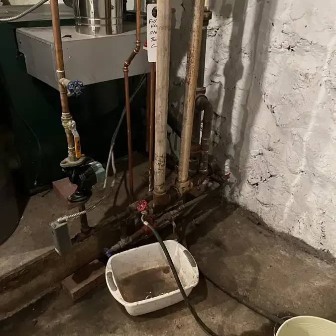 Old boiler piping in a basement corner with buckets catching drips