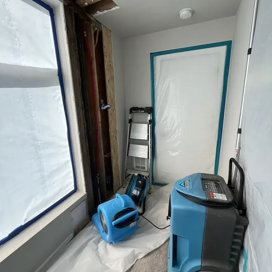 Containment plastic, an air mover and a dehumidifier set up during a dry-out
